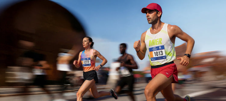 Runners in a race with one wearing a red cap and MIER white tank top.